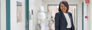 Rashidah Hardwick '15 (M.S.) wears a blazer and white blouse standing in a hallway of Penn Presbyterian Medical Center