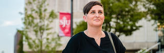 Stephanie Graziosi-Hibbs '16 stands on campus wearing a black top and looking confidently forward