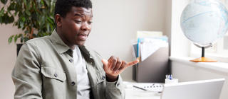 A young man has a conversation using sign language via via meeting on a laptop