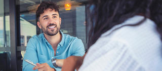 A young, male marketing professional smiles and converses with a coworker.