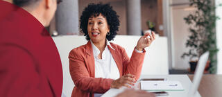 A confident woman has a discussion with a colleague while sitting at a desk