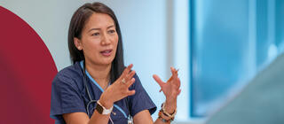 Healthcare professional wearing scrubs speaking to a group of nurses at a table