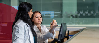 Two pharmacy students parse out pills into a prescription bottle in a lab