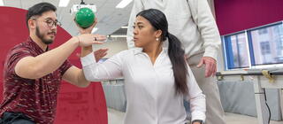 A physical therapy student guides a patient in an arm-focused exercise