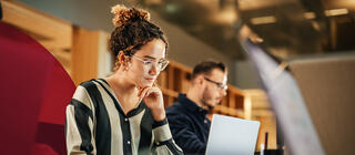 Young woman working on computer in a bright space with others working the background