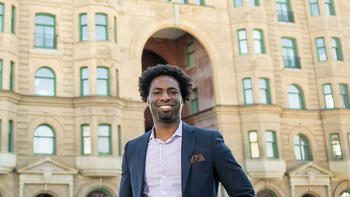 Jameel Rush '14 (M.S.) stands on North Broad Street smiling in a navy blazer